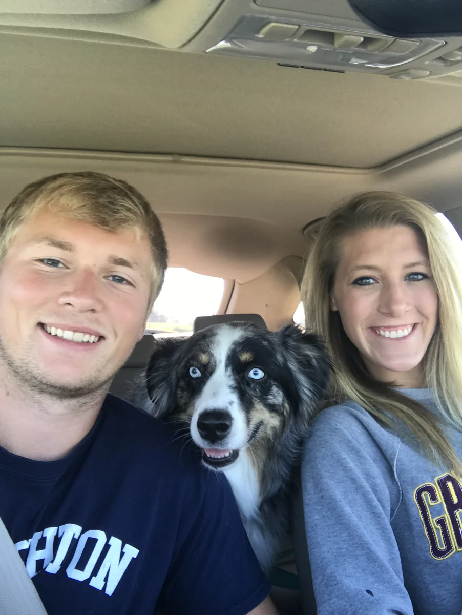 Loki, the Australian Shepherd behind the Longshot name, seated between his owners