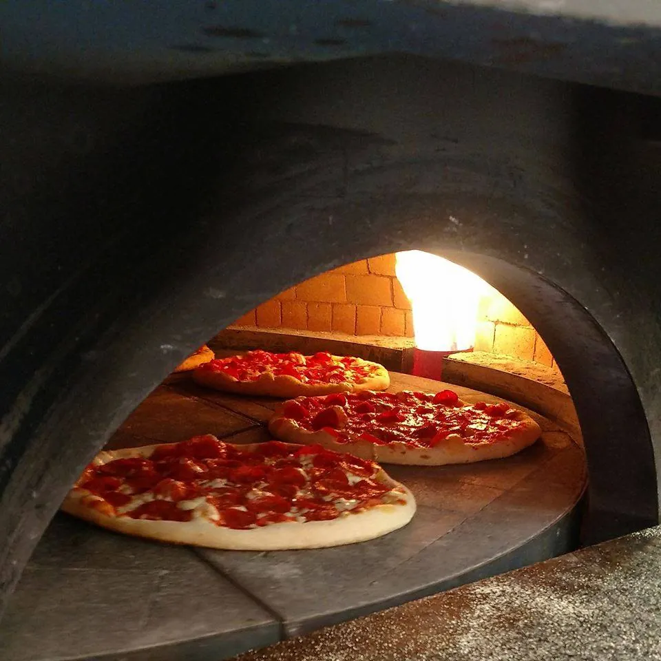 Three pepperoni pizzas baking on the stone deck of the Longshot brick oven