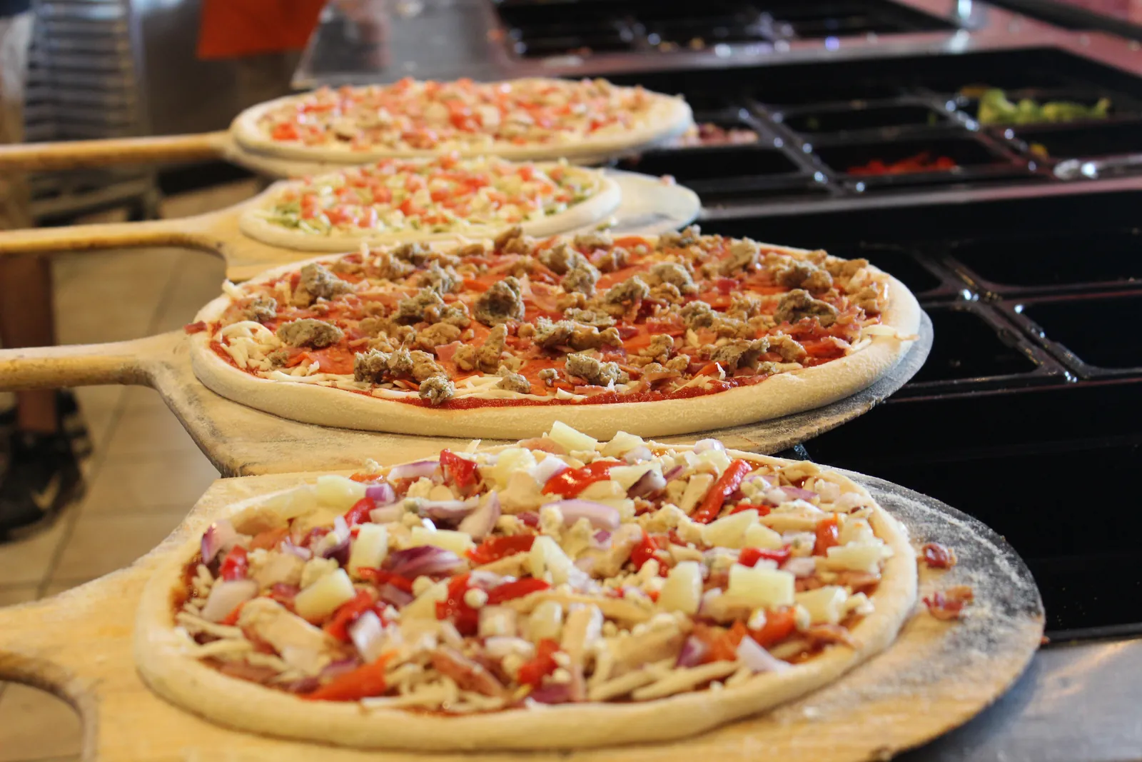 A row of hand-stretched Longshot pizzas topped and waiting on wooden peels beside the make line