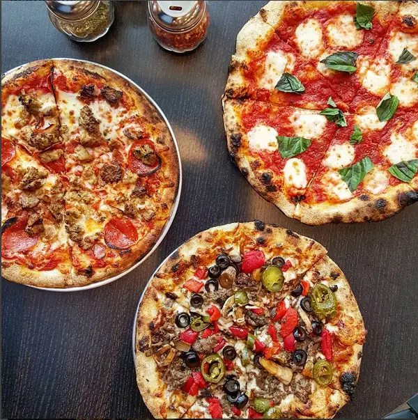 Three Longshot pizzas on a dark table: a meat pie, a margherita and a supreme, each with a blistered brick-oven crust