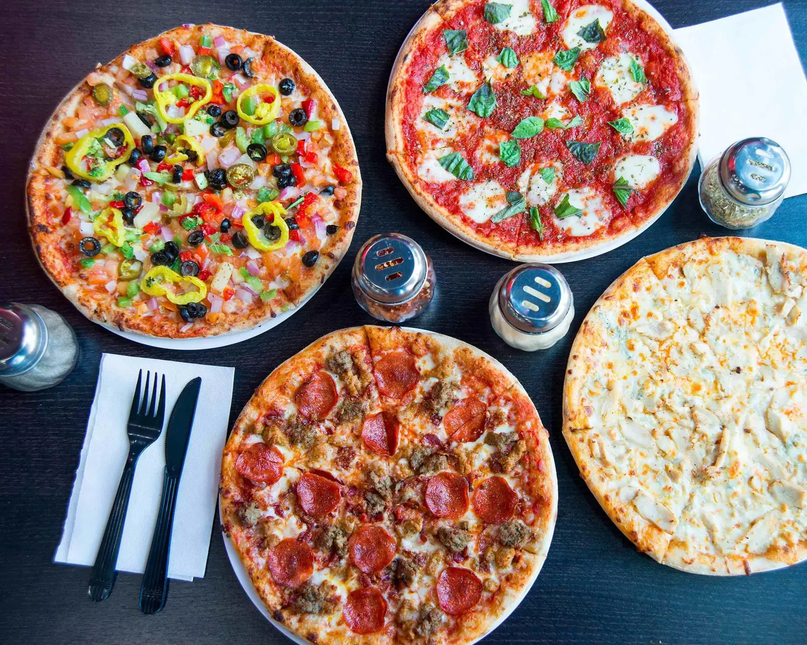 Four Longshot pizzas on a dark table, including a margherita, a pepperoni and sausage, a supreme and a white chicken pie