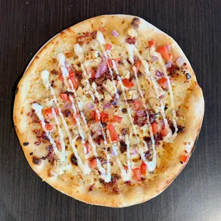 The Rancher, a Longshot specialty pizza seen from above: roasted Garlic Oil, Mozzarella & Provolone, Grilled Chicken, Bacon, Tomato, Red Onion, Ranch Drizzle, on a blistered brick-oven crust