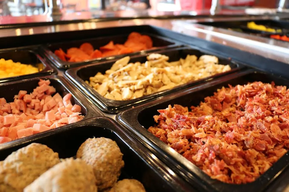 The Longshot topping line: pans of shredded cheddar, pepperoni, grilled chicken, diced ham, chopped bacon and meatballs