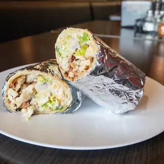The CBR Wrap, halved on a white plate so the filling shows: grilled Chicken, Bacon, Cheddar, Romaine Lettuce, Tomato, Red Onion, Ranch. Served warm in foil or cold.