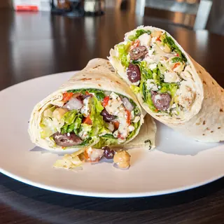 Mediterranean Wrap, halved on a white plate so the filling shows: grilled Chicken, Chickpeas, Feta Cheese, Romaine Lettuce, Spinach, Tomato, Red Onion, Roasted Red Peppers, Kalamata Olives, Greek Vinaigrette, Oregano. Served cold.